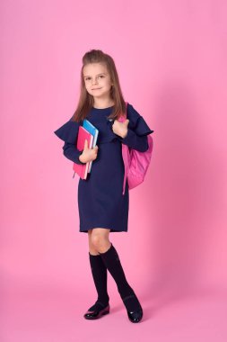 Okul konseptine geri dönelim. Kendine güveni tam, güzel ve zeki bir kızın okul üniforması içinde pembe parlak bir sırt çantası olan yarı dönüştürülmüş fotoğrafı.