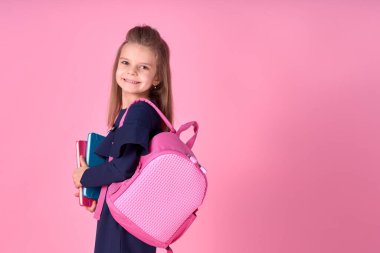 Okul konseptine geri dönelim. Kendine güveni tam, güzel ve zeki bir kızın okul üniforması içinde pembe parlak bir sırt çantası olan yarı dönüştürülmüş fotoğrafı.