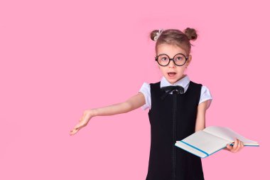 Üniformalı bir ilkokul öğrencisi, gözlüksüz yuvarlak gözlüklü, elinde bir defter tutuyor ve pembe bir arka planda durmakta olan bir sorunun duygusallığıyla elini yana kaldırıyor.