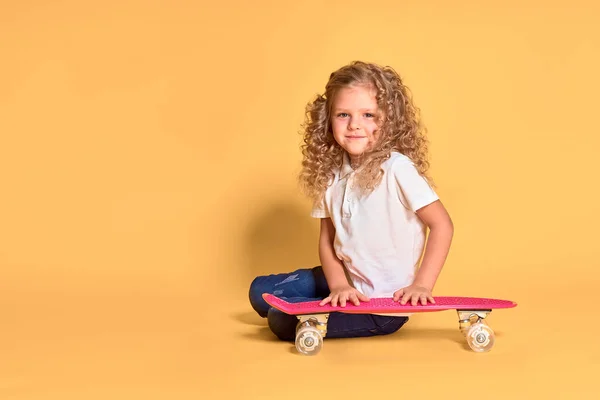 Active and happy girl with curly hair, headphones having fun with penny board, smiling face stand skateboard. Penny board cute skateboard for girls. Lets ride. Girl with penny board yellow background