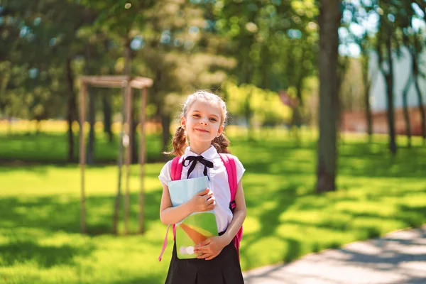 学校のバックパックを着て練習帳を持って笑顔の学生の女の子。小学校の外で幸せな白人の少女の肖像画。笑顔女子高生カメラを見て — ストック写真