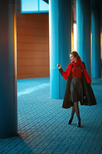 Jong mooi meisje met perfecte make-up, rode lippen, het dragen van een donkere jas, rood shirt, poseren in de buurt winkelcentrum. Ze komt net uit een dure kledingwinkel. — Stockfoto