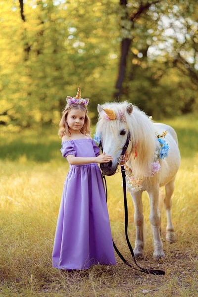 穿着紫色衣服、头戴独角兽花环、头戴白色独角兽马的女孩。梦想成真了童话故事 — 图库照片