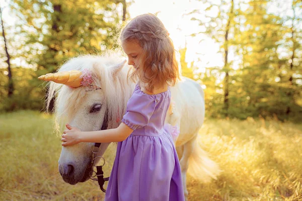 Meisje in paarse jurk knuffelende witte eenhoorn paard. Dromen komen uit. Sprookje — Stockfoto