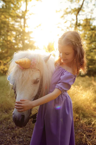 穿着紫色衣服的女孩抱着白色独角兽马。梦想成真了童话故事 — 图库照片