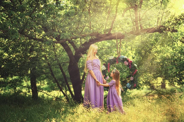 Moda foto ao ar livre de aparência bonita família. bela mãe com longos cabelos escuros posando com seu pequeno bebê bonito em vestidos semelhantes com flores imprimir — Fotografia de Stock