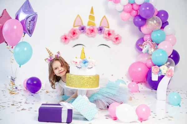 Menina unicórnio posando perto de bolo de aniversário feliz. Ideia para decorar festa de aniversário estilo unicórnio. Decoração de unicórnio para festa menina — Fotografia de Stock