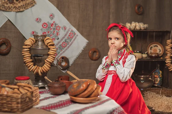 Entzückendes Mädchen, das am Tisch voller Essen und großem Samowar sitzt. Traditionelles Masleniza-Fest — Stockfoto