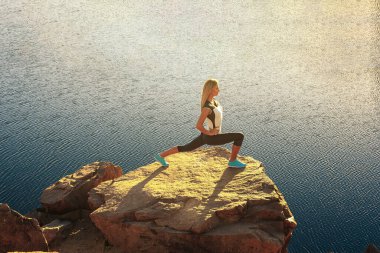 Genç, sıska kadın dağ nehrinin taştan kıyısında yoga yapıyor. Doğa kavramıyla birlik