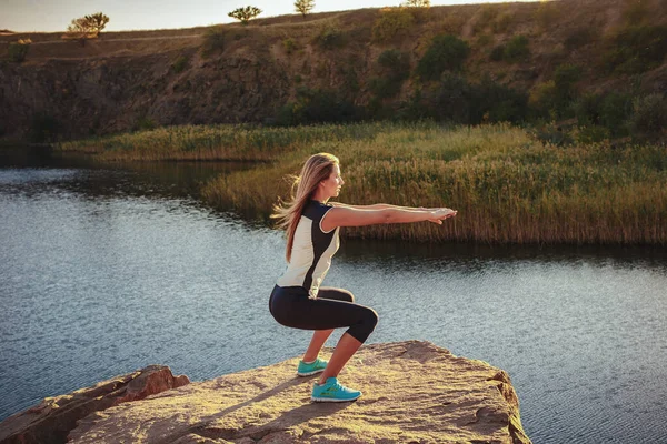 Joven mujer delgada practicando yoga al aire libre en la orilla de piedra del río de montaña. Unidad con el concepto de naturaleza —  Fotos de Stock