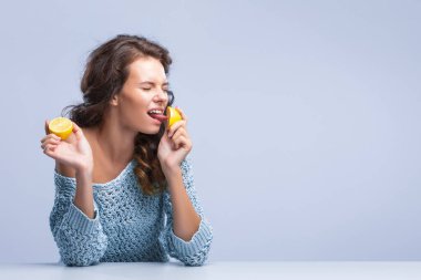 Sevimli esmer kadın elinde iki dilim sarı limonlu narenciye meyve tutuyor ve ilk yarısının iştahını ısırıyor.
