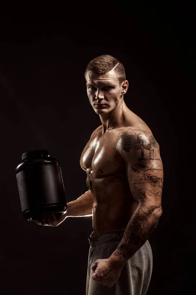 Sport háttér. Erős testépítő, kezében egy műanyag tégely száraz fehérjével izolált. Sport ételek — Stock Fotó