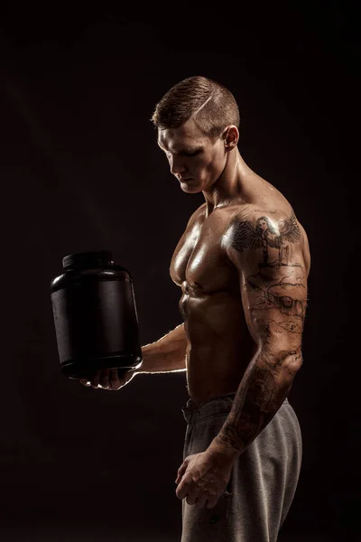 Fundos desportivos. Forte fisiculturista segurando um frasco de plástico com uma proteína seca Isolado. Comida desportiva — Fotografia de Stock