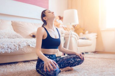 Kadın yoga yapıyor, evde lotus pozisyonunda otururken boyun için jimnastik egzersizleri yapıyor. Online eğitim. Karantinaya alın. Evde kal.