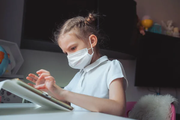 Kaukasiska preteen flicka med medicinsk mask på ansiktet koncentrerade sig på sin uppgift med tablett. Begreppet distansundervisning isolerat medan coronavirus — Stockfoto