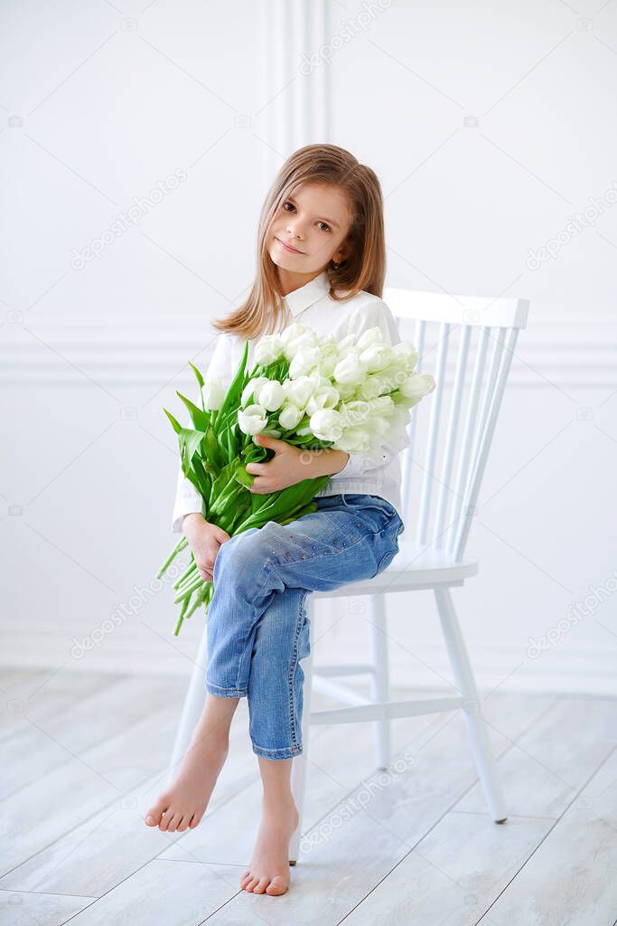 Portrait of beautiful pretty girl with yellow flowers tulips sitting in arm-chair, smiling. Indoor photo