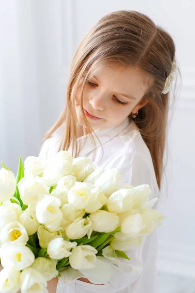 Портрет красивой красивой девушки с белыми цветами тюльпаны сидят на стуле, улыбаясь. Фото в помещении — стоковое фото