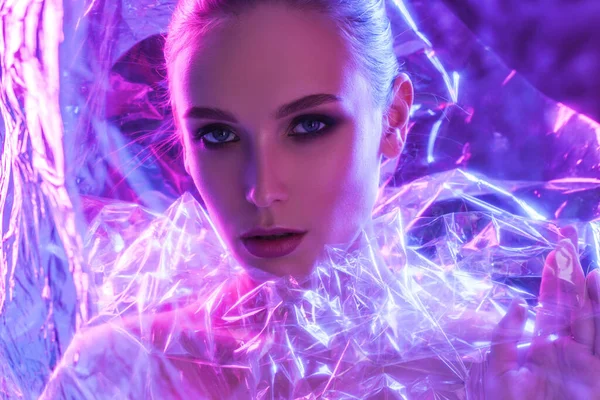 Stüdyoda şeffaf film vasıtasıyla poz veren renkli parlak neon ışıklı model kız. Ultraviyole ışıktaki güzel seksi kadın portresi. Sanat tasarımı renkli makyaj. Renkli ve canlı arkaplanda — Stok fotoğraf