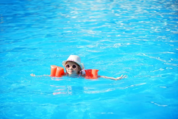 Ein charmantes Kind von europäischem Aussehen, ein Mädchen von 7-8 Jahren, das im Pool schwimmt. Sommer, ein klarer und sonniger Tag. Ein Mädchen mit ihrer Familie im Urlaub auf See. Das Mädchen hat aufblasbare Armrüschen — Stockfoto