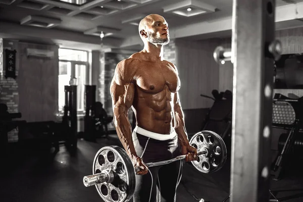 肌肉发达的男人在体育馆里做运动，二头肌上有哑铃，强壮的男性裸体躯干 — 图库照片