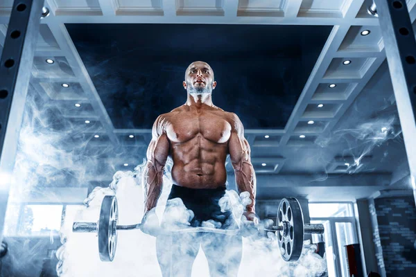 Мускулистый мужчина тренируется в спортзале, делает упражнения с гантелями на бицепсах, сильный мужской обнаженный пресс для туловища — стоковое фото