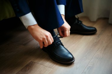 Ahşap bir zeminde bağcıkları siyah ayakkabılara bağlayan adam