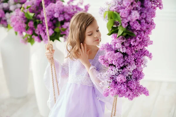 Piękna dziewczynka w wieku przedszkolnym w delikatnej sukience, siedząca na huśtawce ozdobionej kwiatami lilii — Zdjęcie stockowe