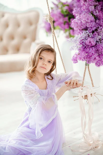 Belle petite fille d'âge préscolaire dans une robe délicate assise sur une balançoire décorée de fleurs de lilas — Photo