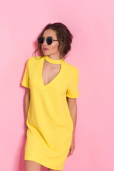 노란 드레스를 입고 스튜디오에서 핑크 색옷을 입고 선글라스를 쓴 아름다운 소녀 — 스톡 사진