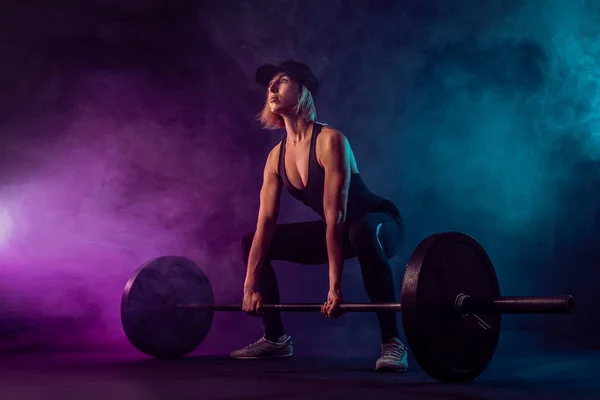 Πλευρική άποψη του γυναικείου bodybuilder κάνει deadlift χρησιμοποιώντας barbell. Srtong γυναίκα με μυϊκό σώμα σε αθλητικά παπούτσια κατάρτισης σε σκοτεινή ατμόσφαιρα. Έννοια του bodybuilding — Φωτογραφία Αρχείου