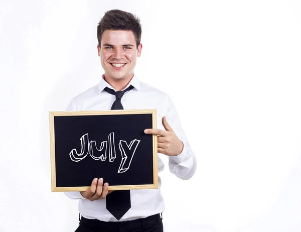 Juillet - Jeune homme d'affaires souriant tenant un tableau noir avec du texte — Photo