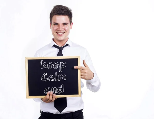 Keep calm and - Young smiling businessman holding chalkboard wit — Stock Photo, Image