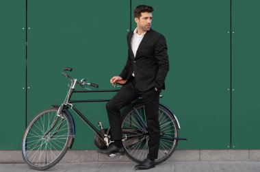 Takım elbiseli genç adam klasik bisikletine yaslanıyor.