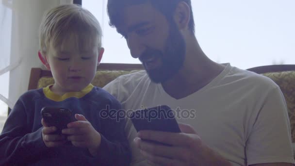 Племянник и дядя вместе играют в игры на телефонах — стоковое видео