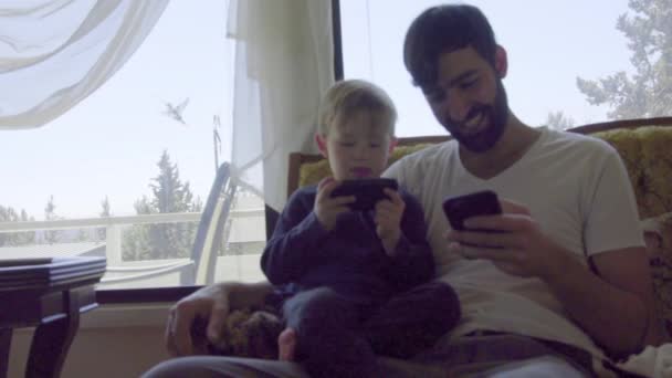 Střední záběr mladého chlapce a muže hrát na jejich mobilní telefony — Stock video