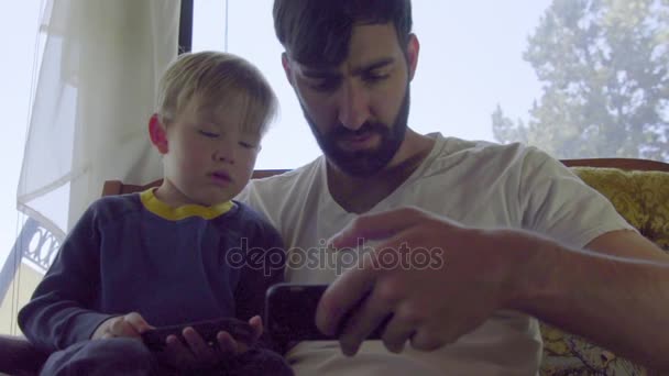 Un joven y un niño miran juntos un celular. — Vídeos de Stock