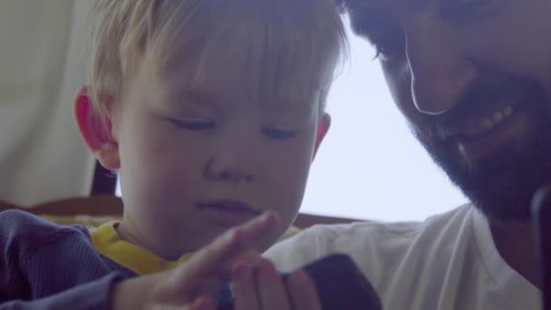Tio se senta com seu sobrinho enquanto ele joga em um telefone celular — Vídeo de Stock