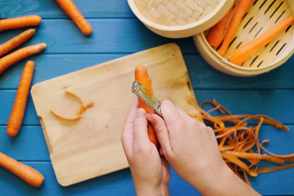 Turuncu bir havuç mavi arka plan üzerinde peeling eller