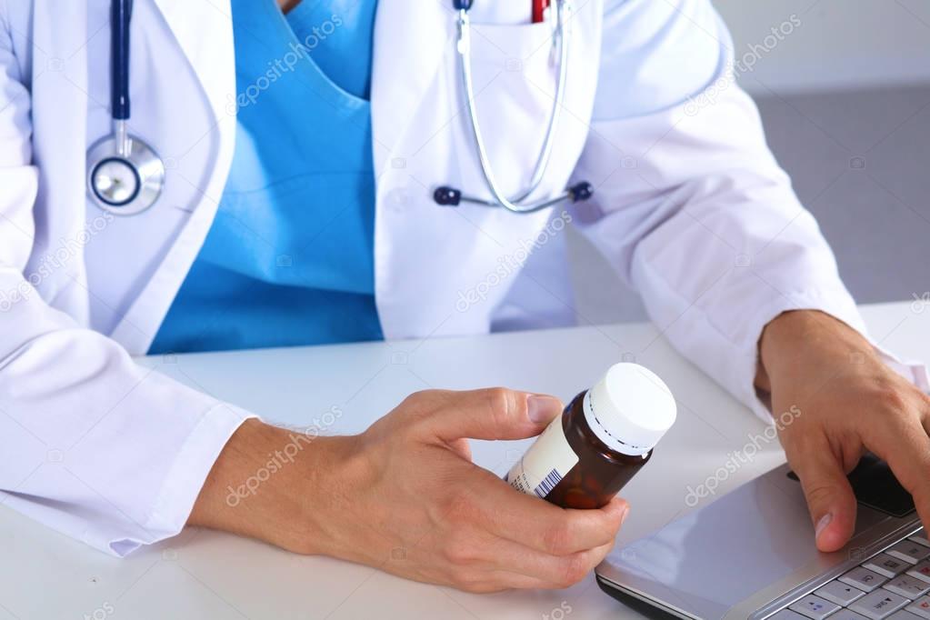 Male medicine doctor hands hold jar of pills and type something on laptop computer keyboard. Panacea  life save, prescribing treatment, legal drug store, take stock, consumption statistics concept