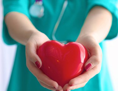 Genç kadın doktor ofisinde kırmızı bir kalp tutan