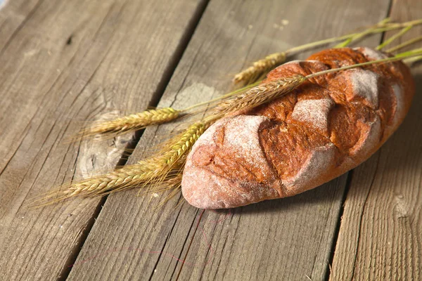 Rustic crusty bread and wheat ears on a dark wooden table — Stock Photo, Image