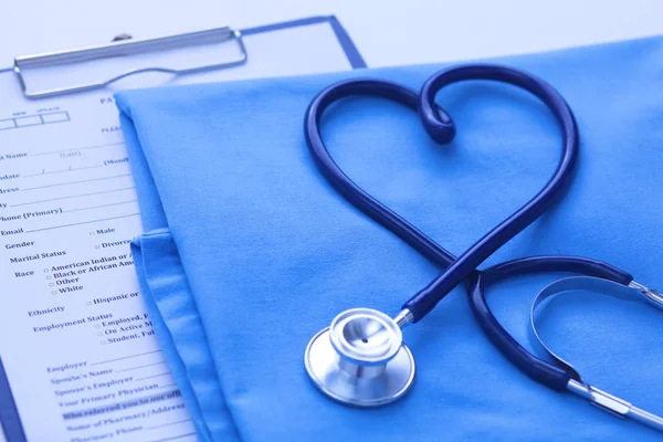 Estetoscopio médico retorcido en forma de corazón que se encuentra en la lista de antecedentes médicos del paciente y el primer plano uniforme médico azul. Ayuda médica o concepto de seguro. Atención cardiológica, salud, protección y prevención —  Fotos de Stock