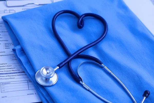 Zdravotní stetoskop stočeny do tvaru srdce leží na seznamu pacienta anamnézu a modré doktor jednotné closeup. Lékařskou pomoc nebo pojištění konceptu. Kardiologická péče, zdraví, ochrana a prevence — Stock fotografie