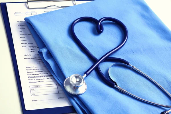 Stetoskop medis memutar dalam bentuk hati terletak pada daftar riwayat medis pasien dan penutupan seragam dokter biru. Bantuan medis atau konsep asuransi. Perawatan kardiologi, kesehatan, perlindungan dan pencegahan — Stok Foto