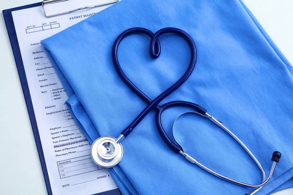 Estetoscópio médico torcido em forma de coração deitado na lista de história médica do paciente e médico azul uniforme closeup. Conceito de ajuda médica ou seguro. Cuidados de cardiologia, saúde, proteção e prevenção — Fotografia de Stock