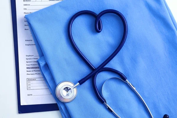 Estetoscópio médico torcido em forma de coração deitado na lista de história médica do paciente e médico azul uniforme closeup. Conceito de ajuda médica ou seguro. Cuidados de cardiologia, saúde, proteção e prevenção — Fotografia de Stock