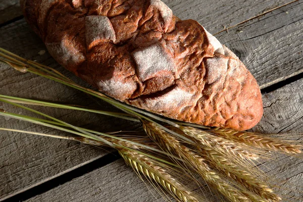 Rustic crusty bread and wheat ears on a dark wooden table — Stock Photo, Image