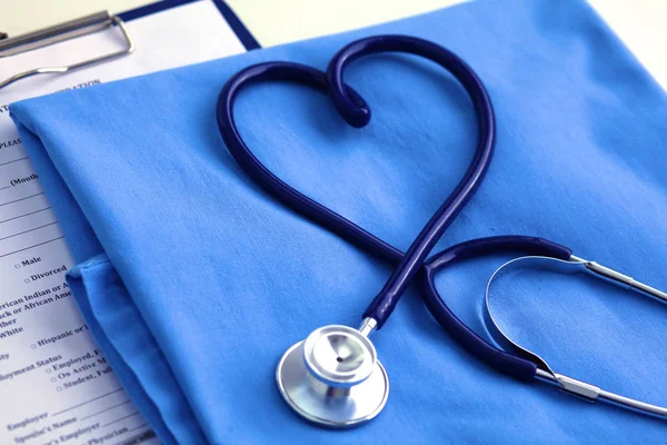 Estetoscopio médico retorcido en forma de corazón que se encuentra en la lista de antecedentes médicos del paciente y el primer plano uniforme médico azul. Ayuda médica o concepto de seguro. Atención cardiológica, salud, protección y prevención —  Fotos de Stock