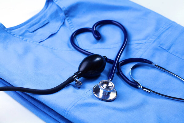 Медицинский стетоскоп скрученный в форме сердца, лежащий в списке пациентов и синей униформе врача крупным планом
