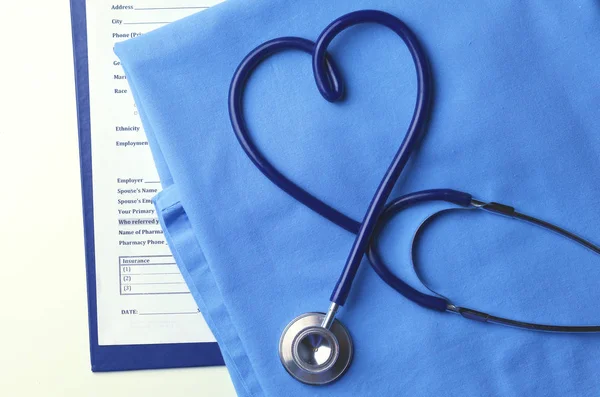 Estetoscopio médico retorcido en forma de corazón que se encuentra en la lista de antecedentes médicos del paciente y primer plano uniforme médico azul —  Fotos de Stock